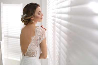 Young bride with elegant wedding hairstyle near window indoors