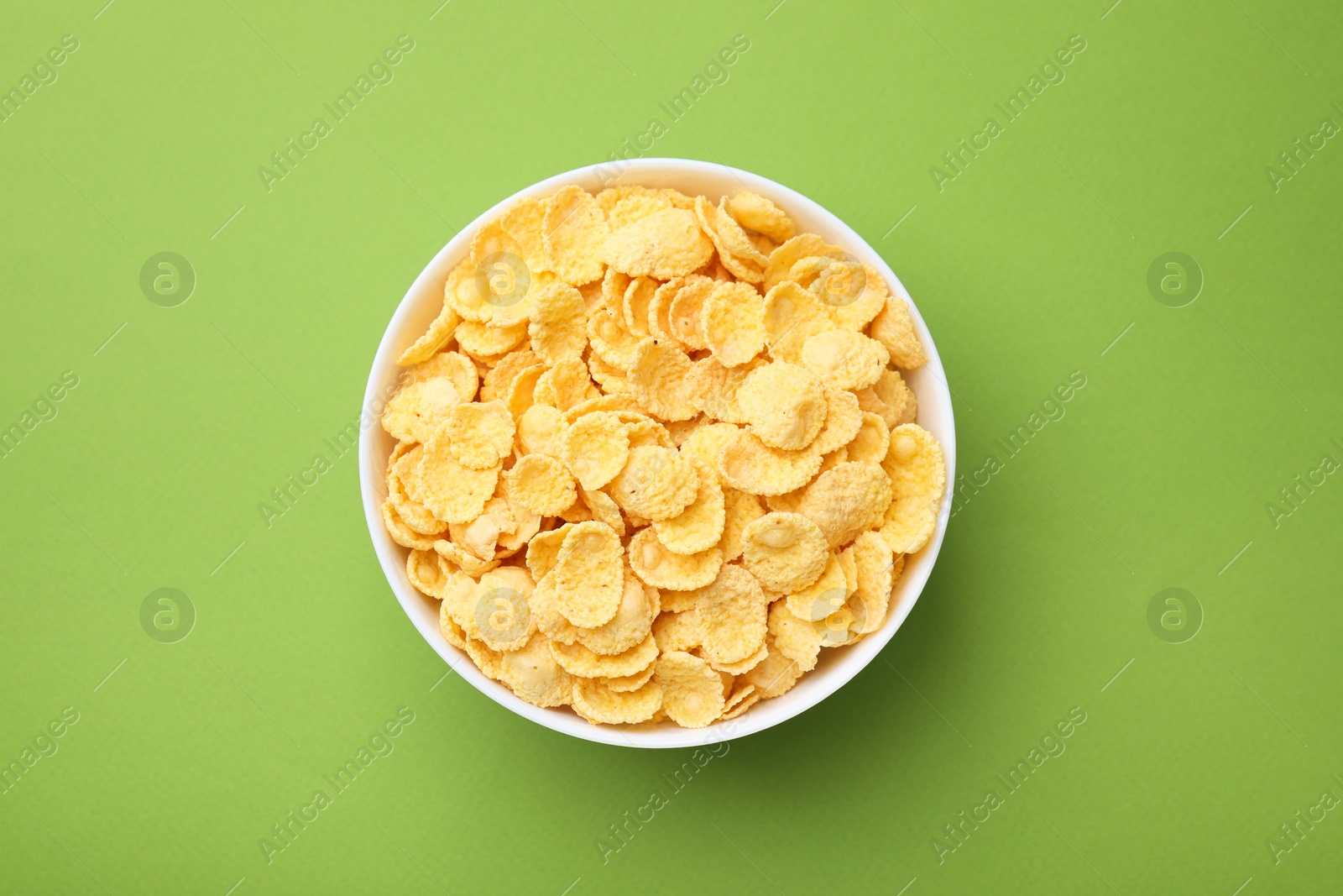 Photo of Breakfast cereal. Tasty corn flakes in bowl on green table, top view