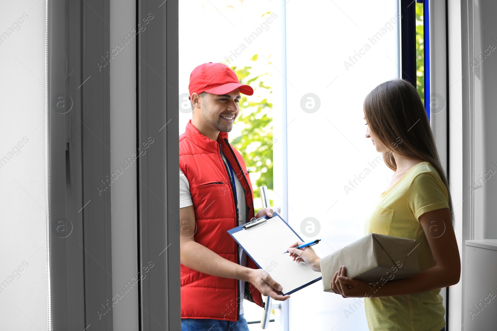 Photo of Woman signing for delivered parcel on doorstep. Courier service