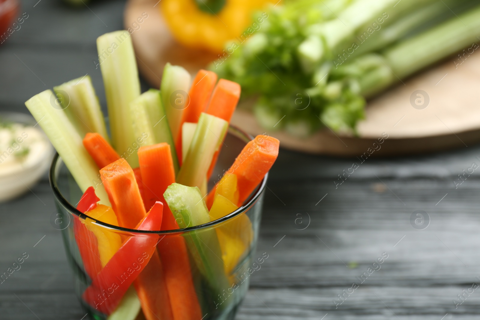 Photo of Celery and other vegetable sticks in glass on grey wooden table, closeup. Space for text