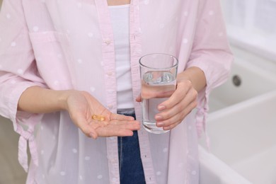 Woman with vitamin pills and glass of water indoors, closeup