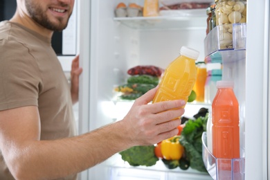 Man taking bottle with juice out of refrigerator in kitchen, closeup