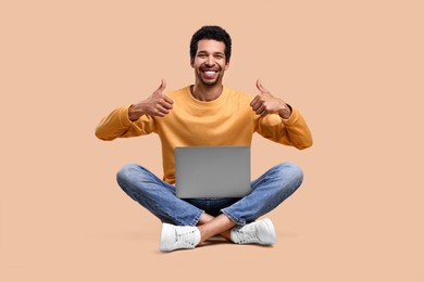 Photo of Happy man with laptop showing thumbs up on beige background