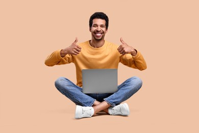 Happy man with laptop showing thumbs up on beige background