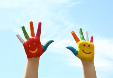 Kid with smiling faces drawn on palms against blue sky, closeup