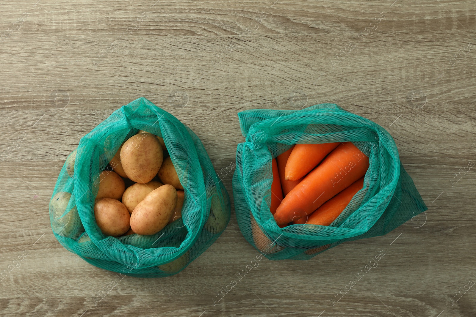 Photo of Net bags with vegetables on wooden table, flat lay