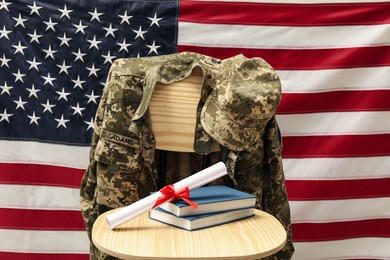 Photo of Diploma, books and soldier uniform on wooden chair near flag of United States. Military education