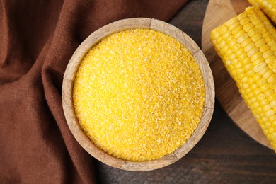 Photo of Raw cornmeal in bowl and corn cob on wooden table, top view