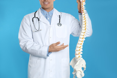 Photo of Male orthopedist with human spine model against blue background, closeup