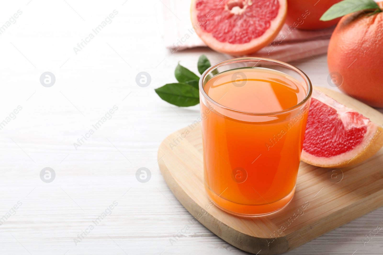 Photo of Tasty freshly made grapefruit juice on white wooden table. Space for text