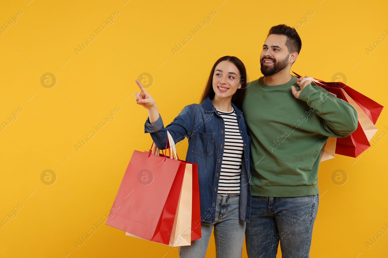 Photo of Happy couple with shopping bags looking at something on orange background. Space for text