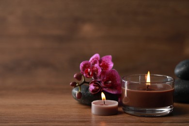 Beautiful spa composition with burning candles and flowers on wooden table. Space for text