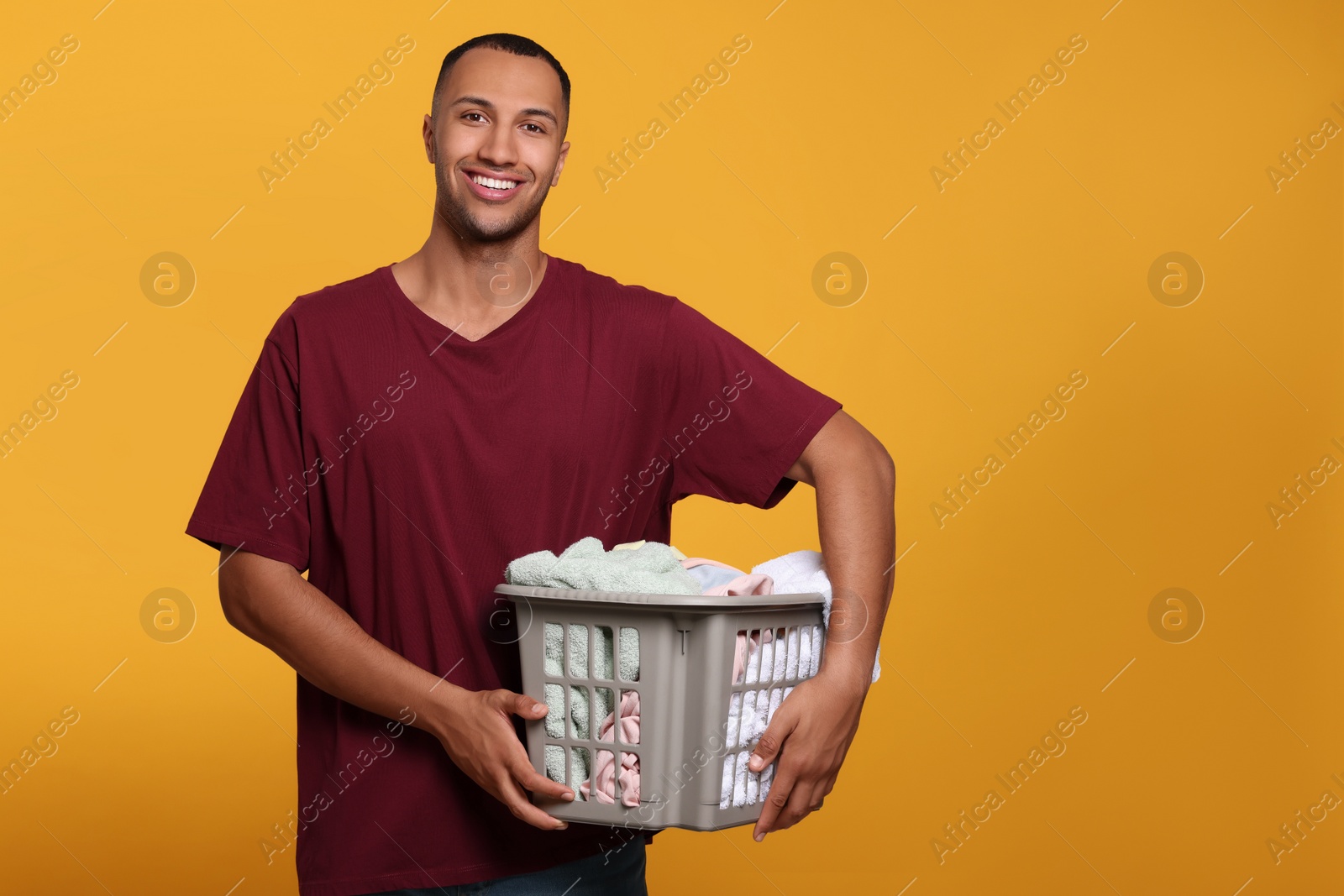 Photo of Happy man with basket full of laundry on orange background. Space for text