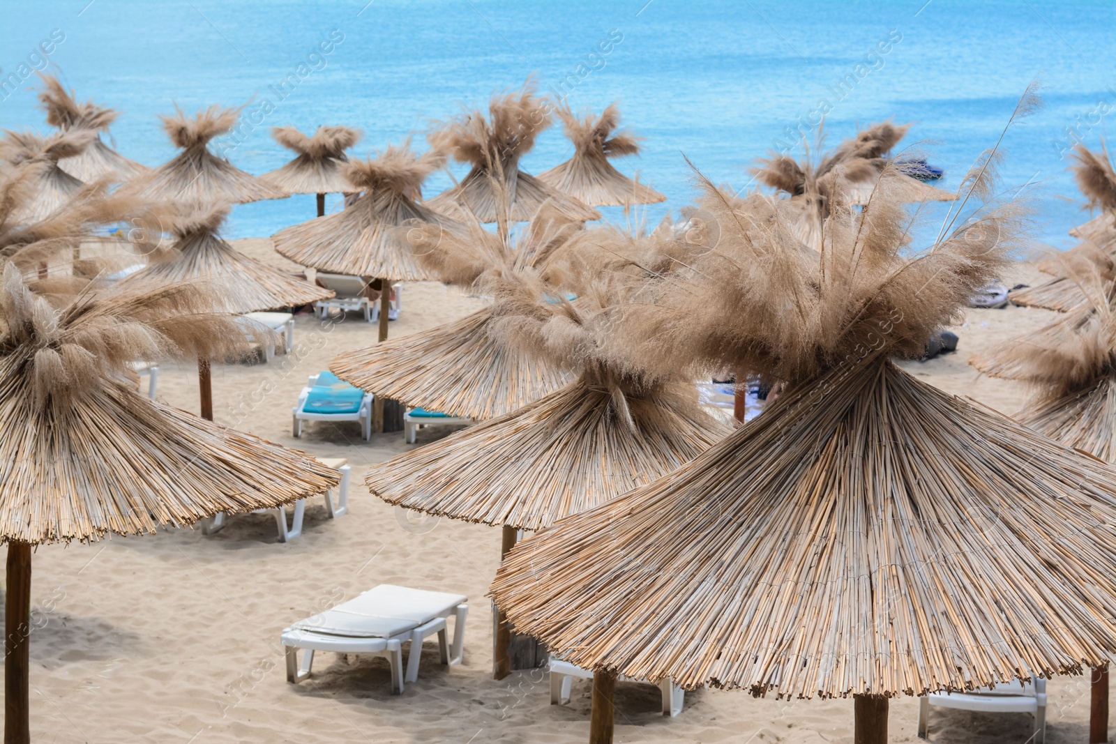 Photo of Beautiful straw umbrellas and sunbeds on beach near sea