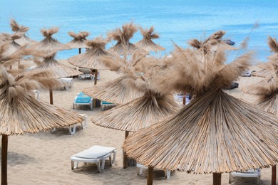 Beautiful straw umbrellas and sunbeds on beach near sea