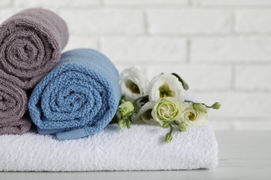 Photo of Rolled and folded towels with flowers on white table, closeup. Space for text