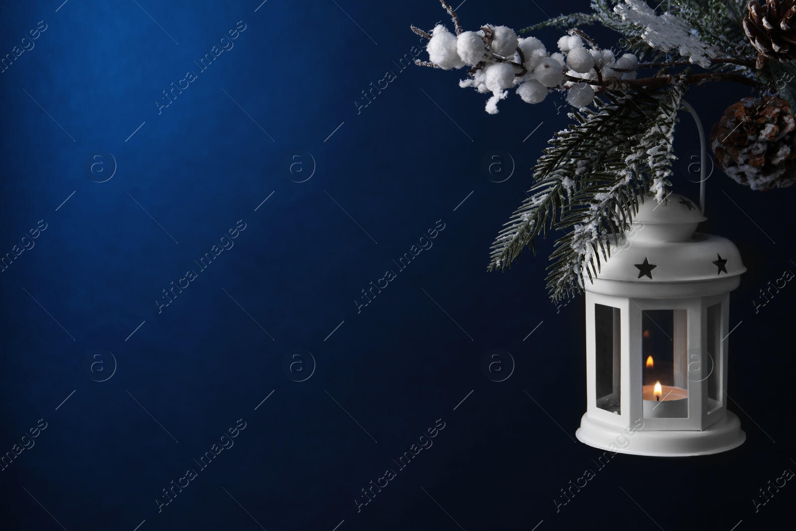 Photo of Christmas lantern with burning candle on fir tree against blue background, closeup. Space for text