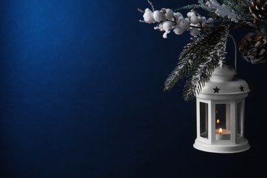 Photo of Christmas lantern with burning candle on fir tree against blue background, closeup. Space for text