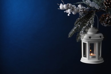 Christmas lantern with burning candle on fir tree against blue background, closeup. Space for text