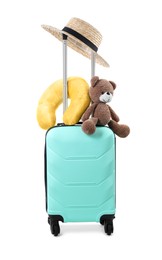 Photo of Soft travel pillow, toy bear and hat on turquoise suitcase isolated on white