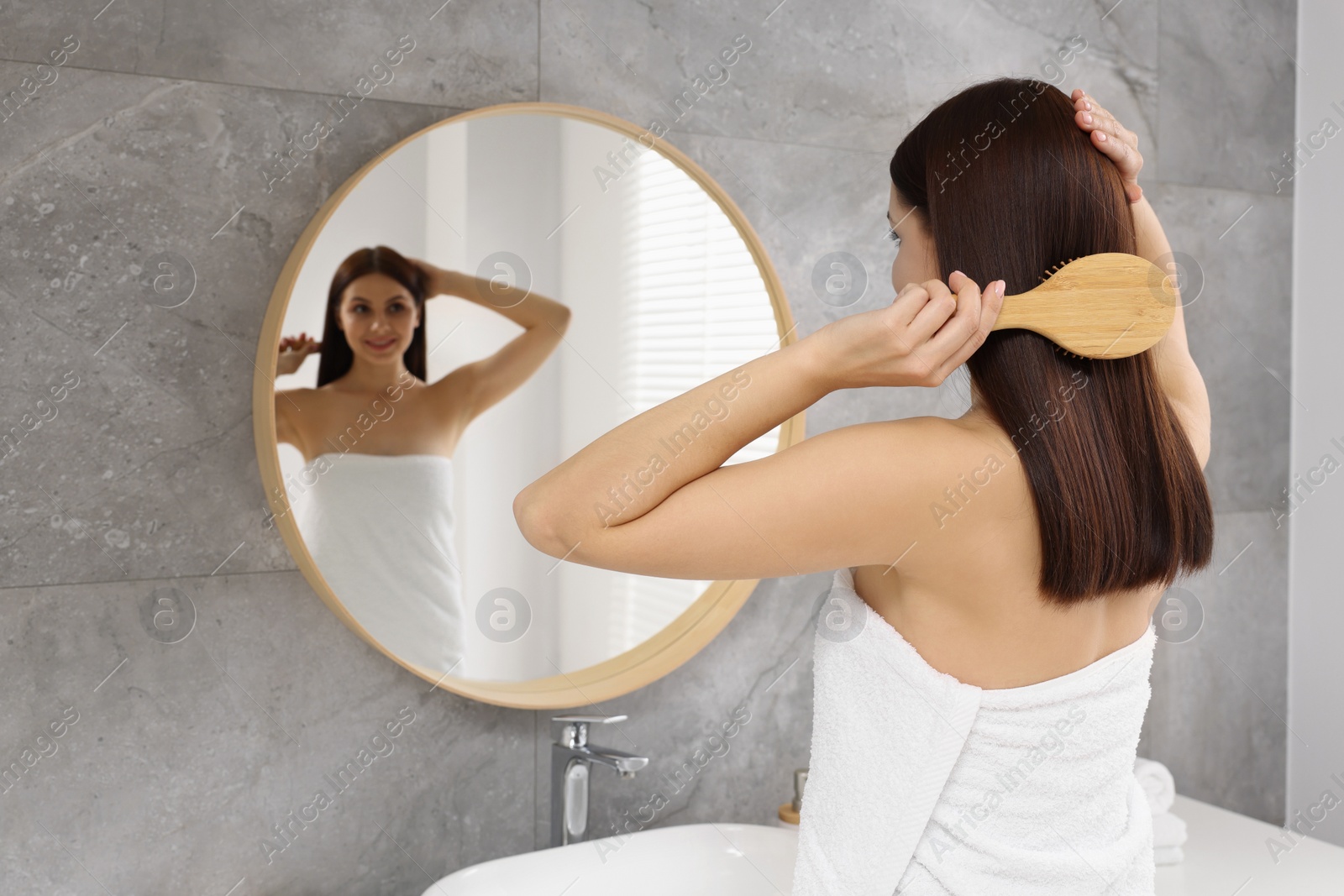 Photo of Beautiful woman brushing her hair near mirror in bathroom