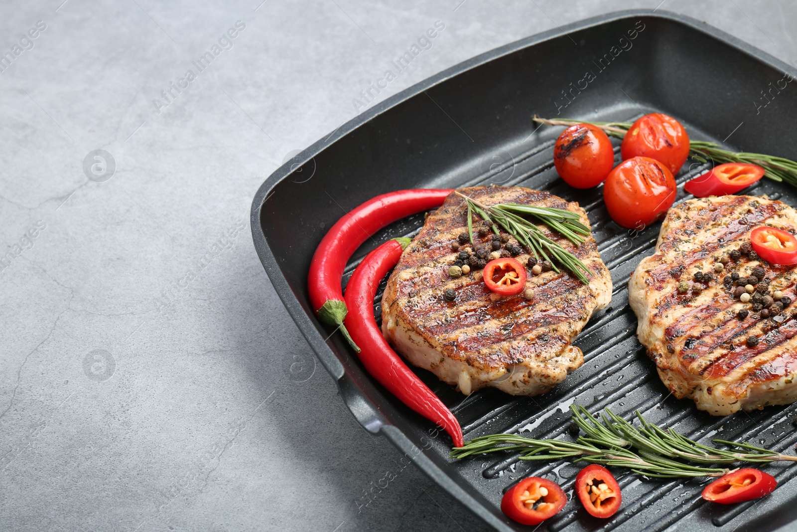 Photo of Grill pan with delicious pork steaks, spices and vegetables on grey table, space for text