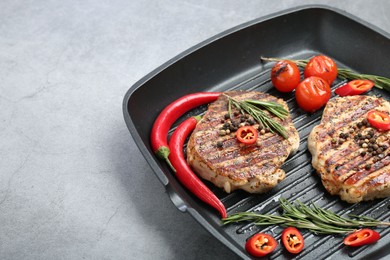 Photo of Grill pan with delicious pork steaks, spices and vegetables on grey table, space for text