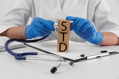 Photo of Doctor and wooden cubes with abbreviation STD at white table, closeup