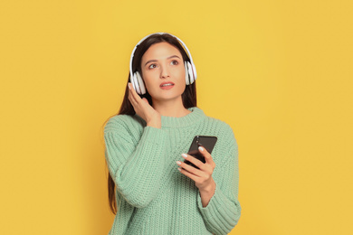 Young woman listening to audiobook on yellow background