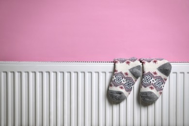 Modern radiator with knitted socks near pink wall indoors, space for text