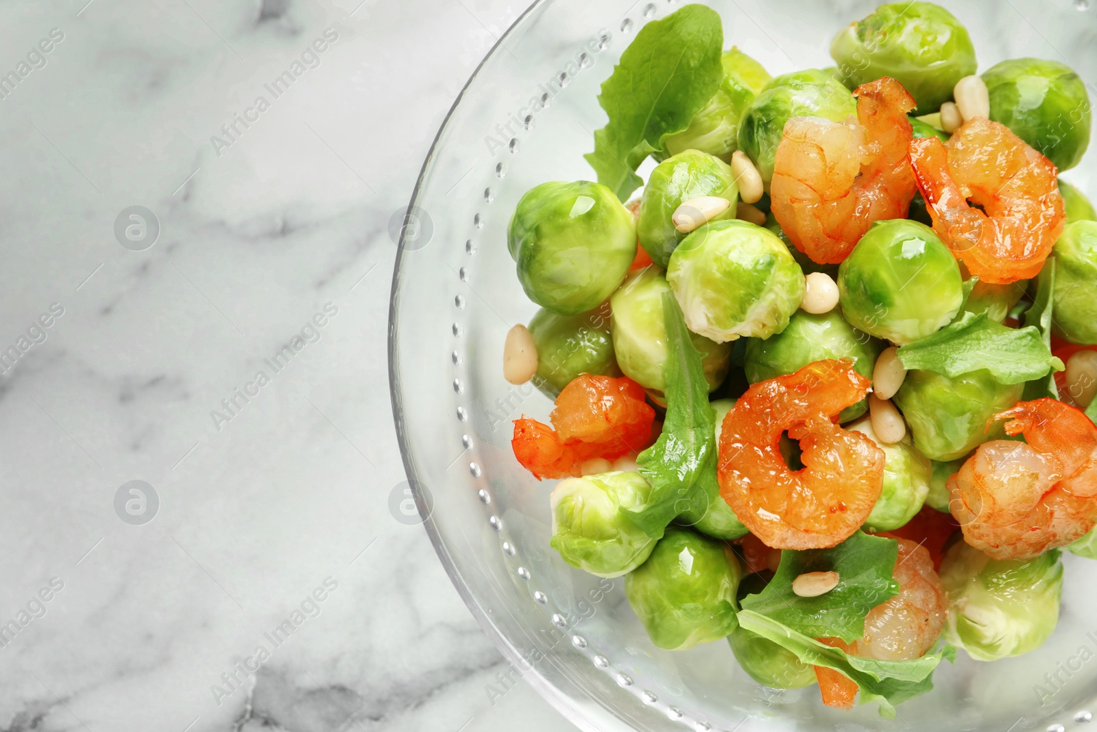 Photo of Bowl of delicious salad with Brussels sprouts and shrimps on marble table, top view. Space for text