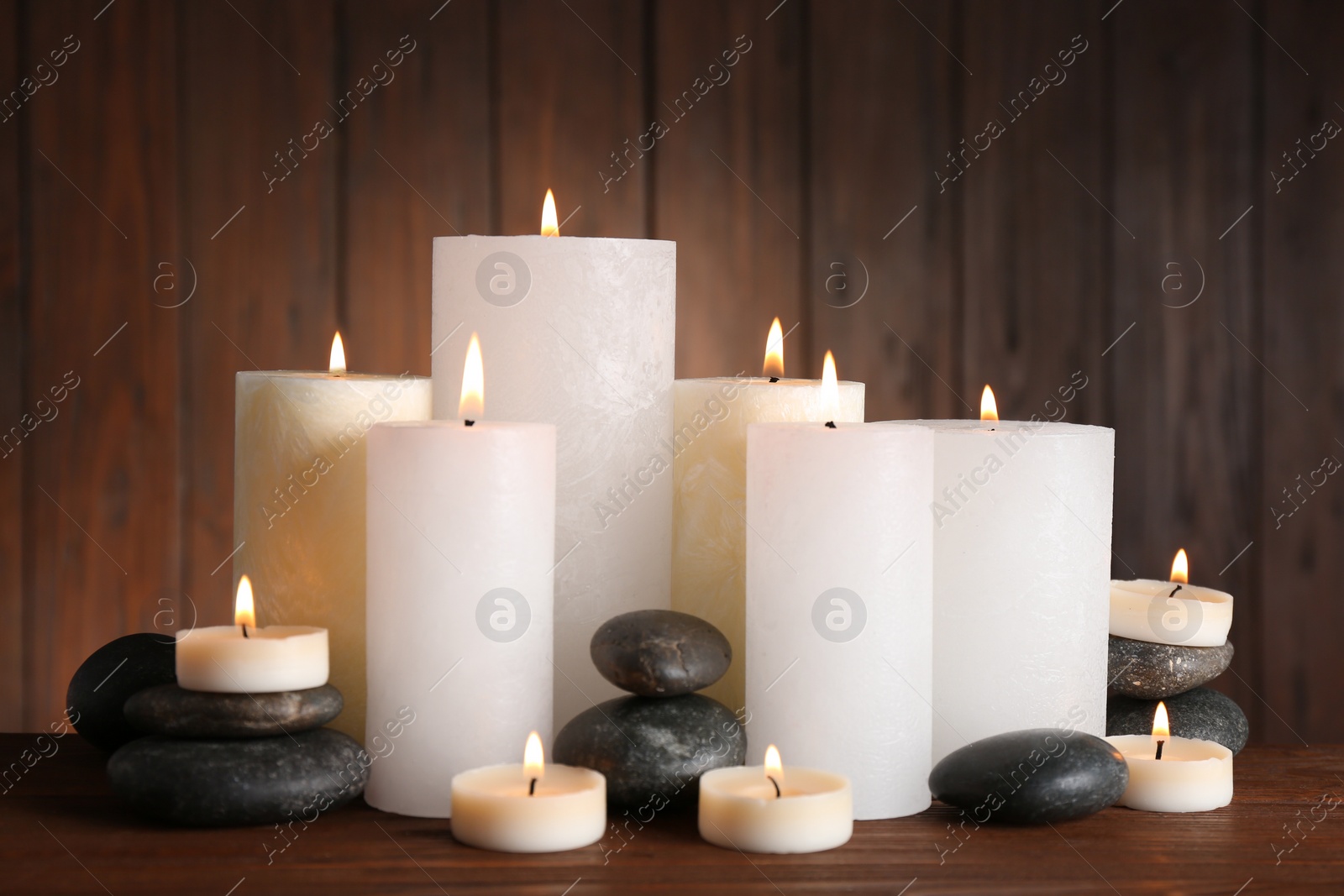 Photo of Beautiful composition with candles and stones on table against wooden background