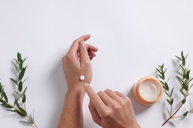 Photo of Woman applying cosmetic cream onto hand on white background, top view