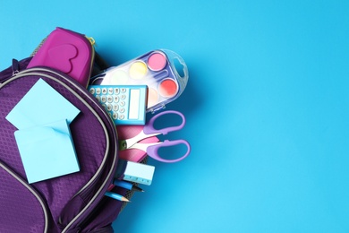 Photo of Purple backpack with different stationery on light blue background, top view and space for text. Back to school