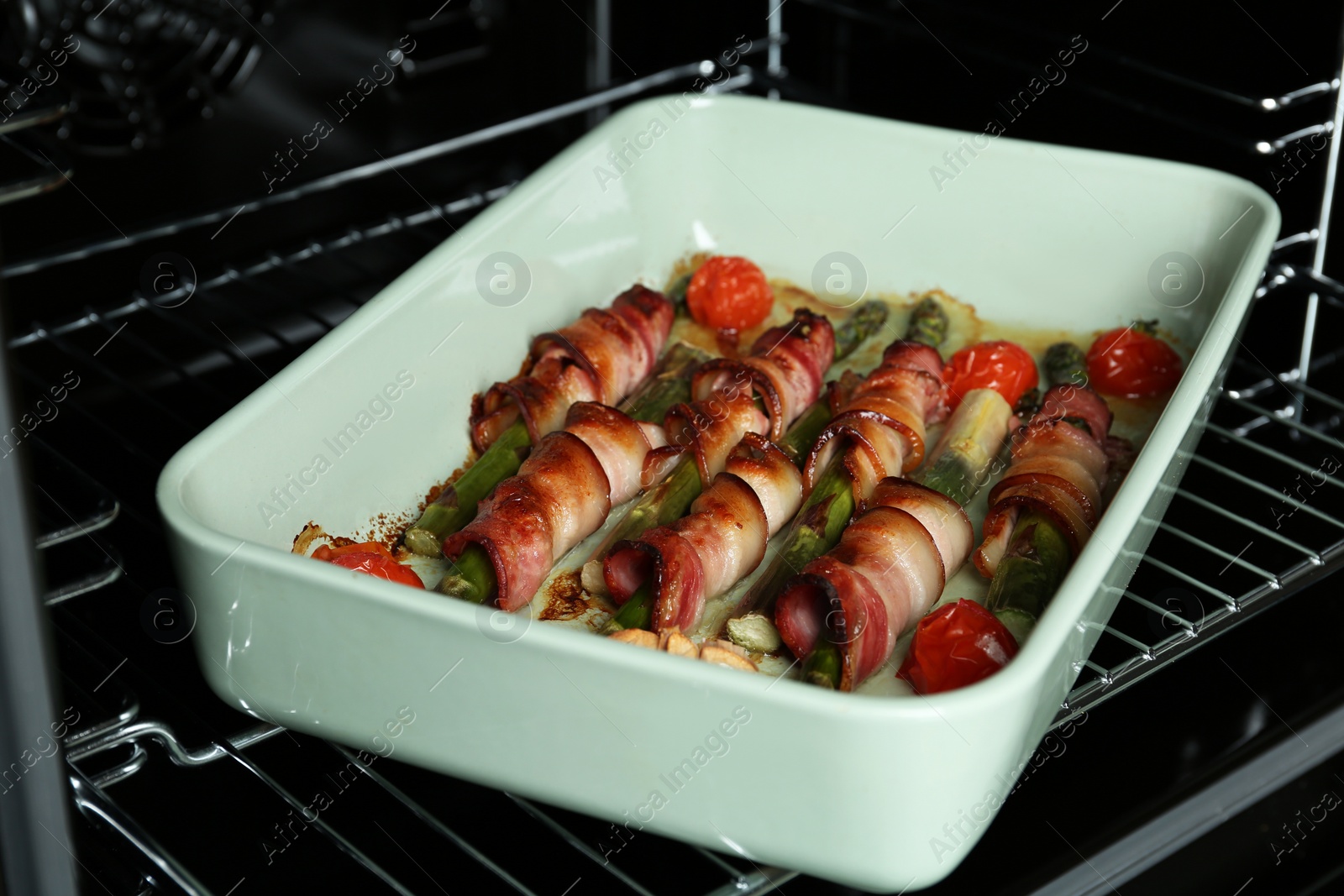 Photo of Bacon wrapped asparagus in baking dish on oven rack, closeup