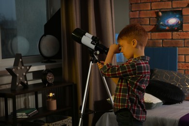 Little boy looking at stars through telescope in room