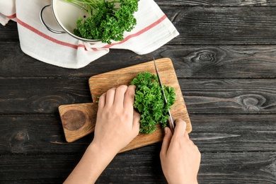 Photo of Woman cutting fresh green parsley at dark wooden table, top view
