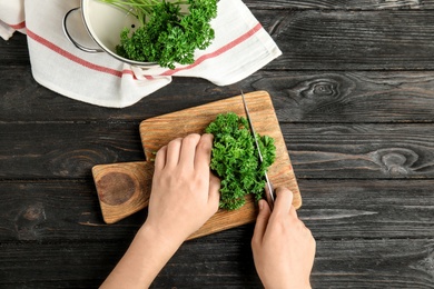 Woman cutting fresh green parsley at dark wooden table, top view