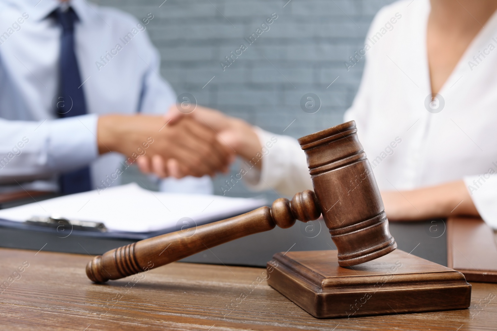 Photo of Wooden gavel and blurred lawyer with client on background