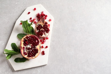 Photo of Board with ripe pomegranates and seeds on grey background, top view. Space for text