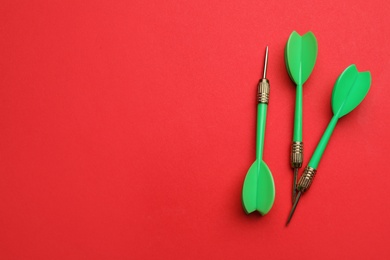 Photo of Green dart arrows on red background, flat lay with space for text