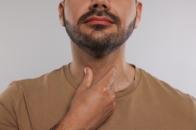 Endocrine system. Man doing thyroid self examination on light grey background, closeup