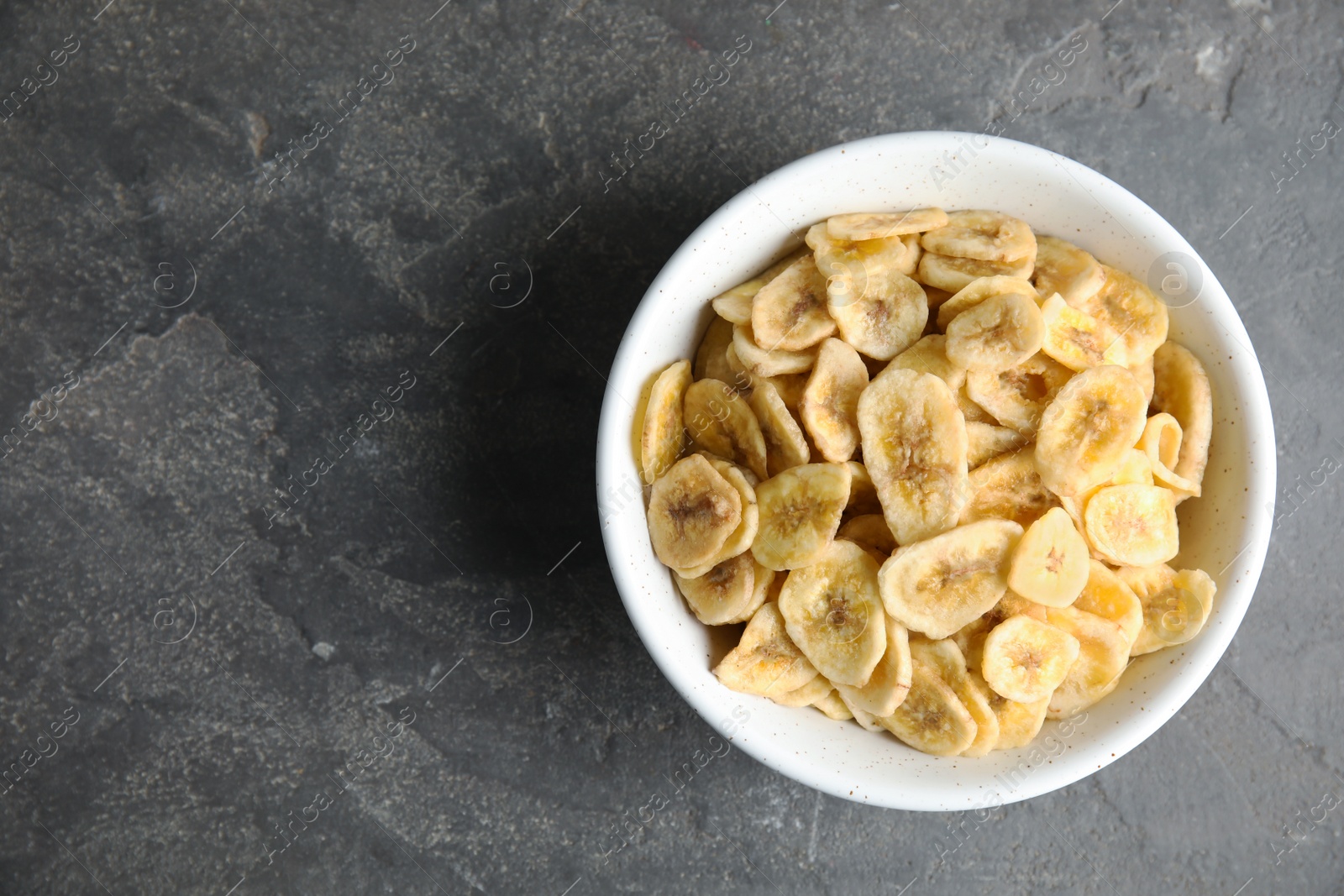 Photo of Bowl with sweet banana slices on grey background, top view with space for text. Dried fruit as healthy snack