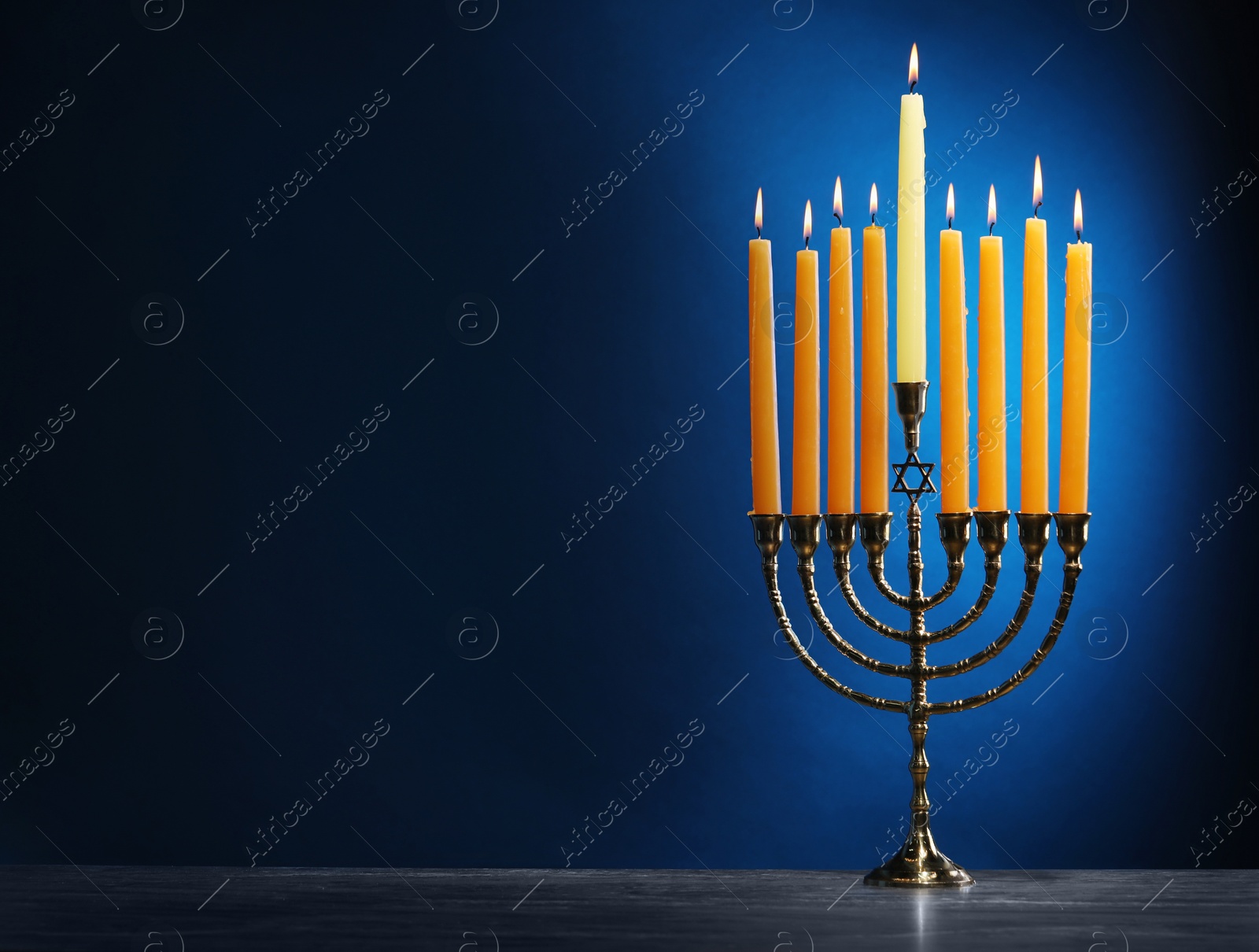 Photo of Hanukkah celebration. Menorah with burning candles on table against blue background, space for text
