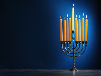 Photo of Hanukkah celebration. Menorah with burning candles on table against blue background, space for text