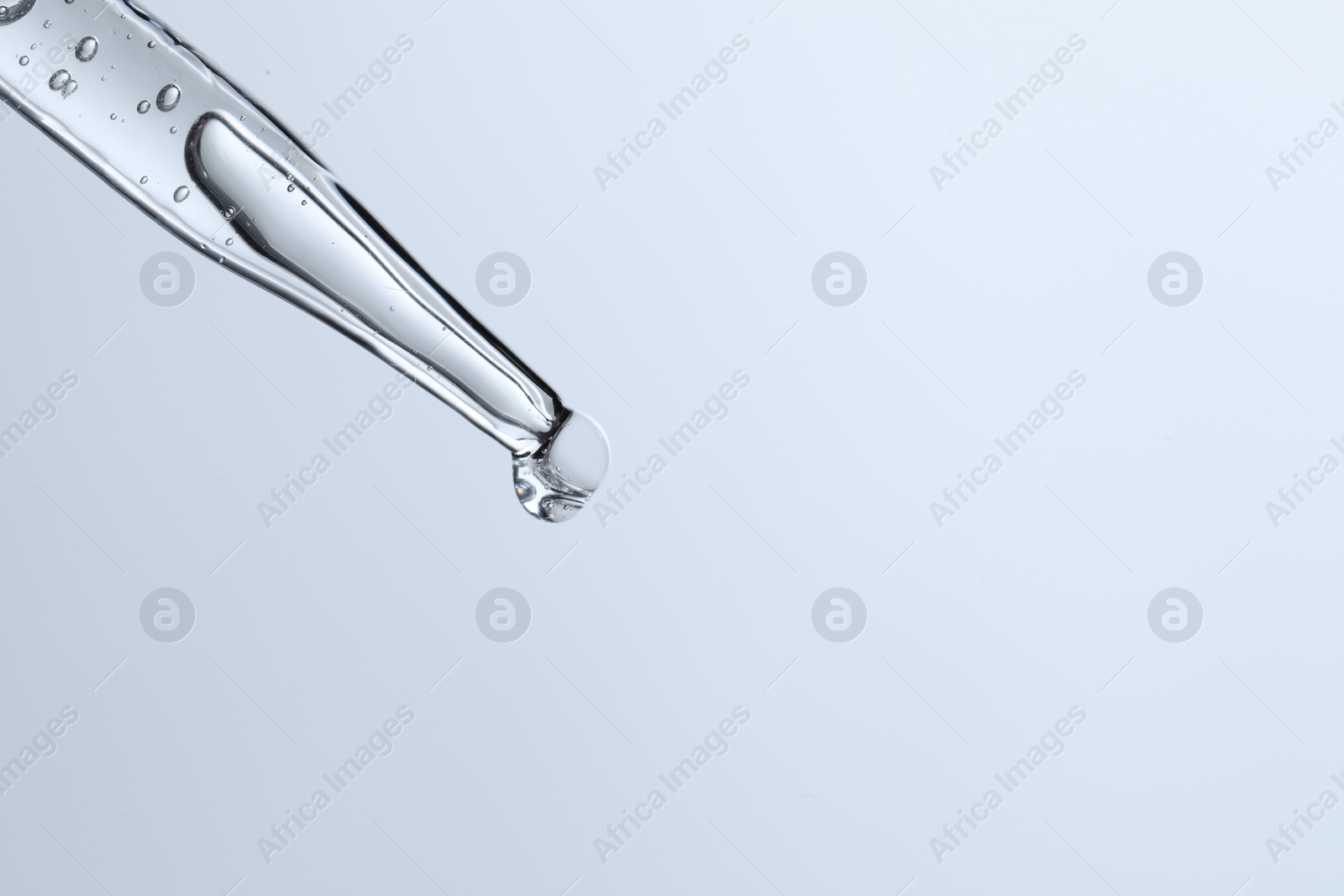 Photo of Dripping liquid from pipette on light blue background, closeup. Space for text