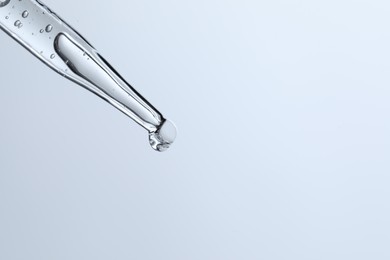 Photo of Dripping liquid from pipette on light blue background, closeup. Space for text