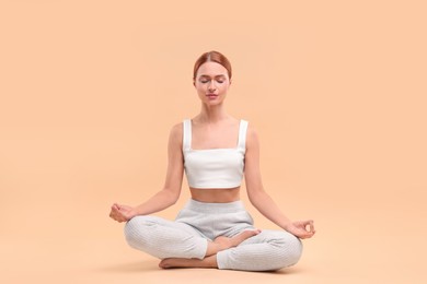 Beautiful young woman practicing yoga on beige background. Lotus pose