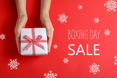 Woman with gift and text Boxing Day Sale on red background, top view