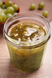 Jar of delicious gooseberry jam and fresh berries on wooden table, closeup